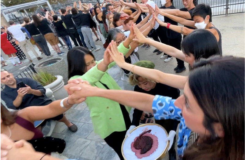 The artist is pictured walking through a crowd of people holding their placenta