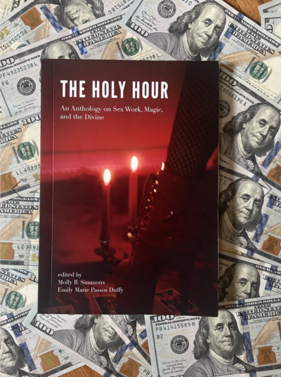 100 dollar bills cover a surface, and atop the bills is a paperback copy of "The Holy Hour An Anthology on Sex Work, Magic, and the Divine"